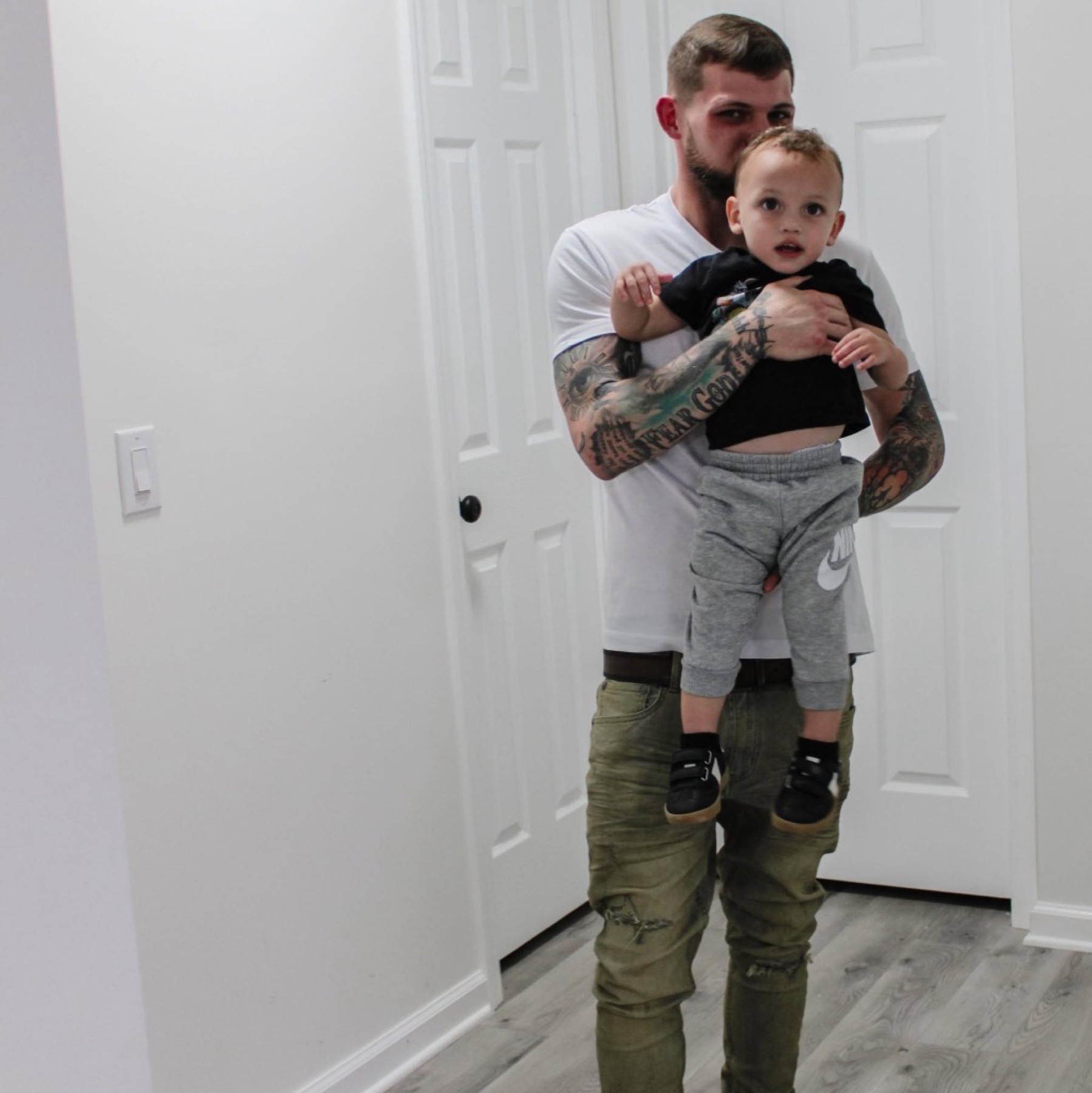 Logan holding his son Grayson in a bright hallway at home